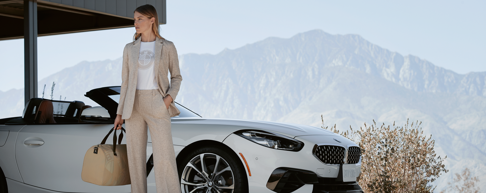 Woman standing by a white BMW car parked with a mountain view