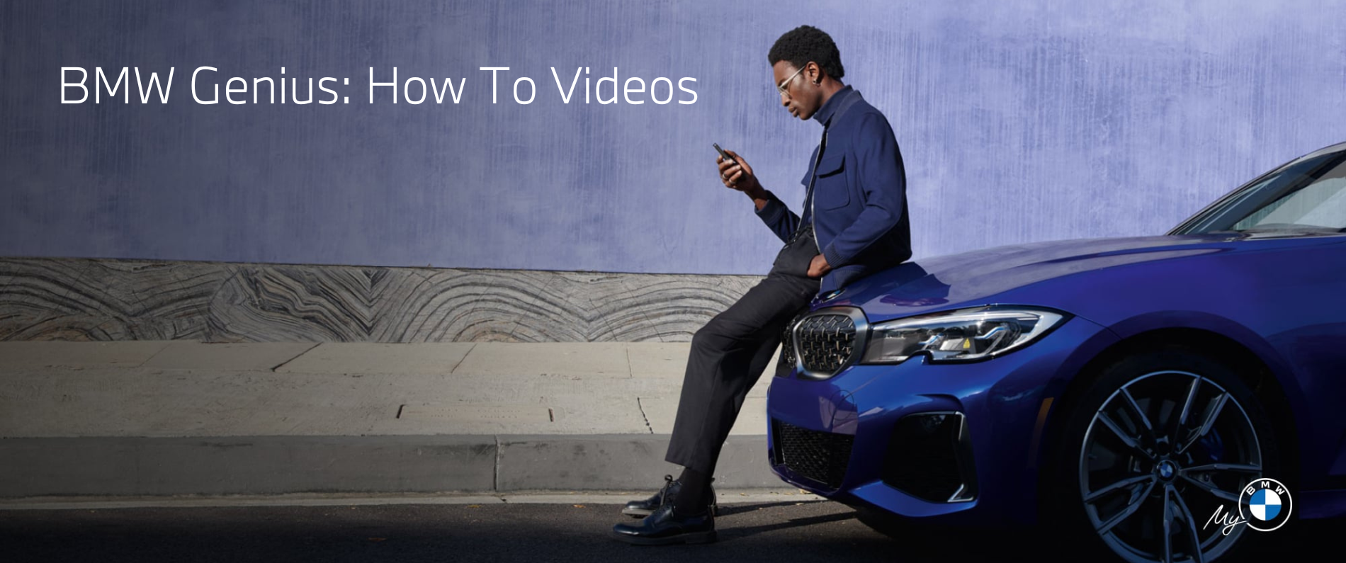 Man leaning on the hood of a BMW looking ad his phone